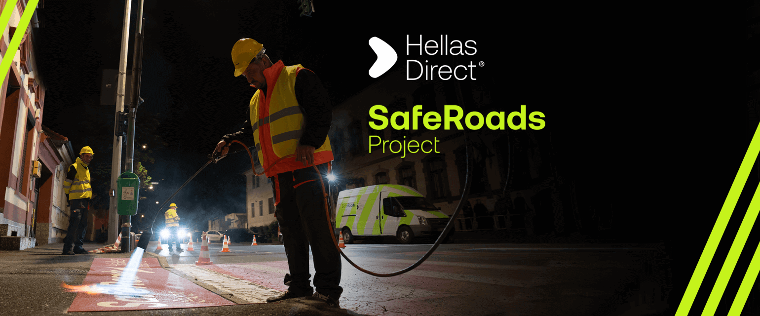 man in yellow vest paints crosswalk outside a school in the night. Written text: Hellas Direct, Safe Roads project